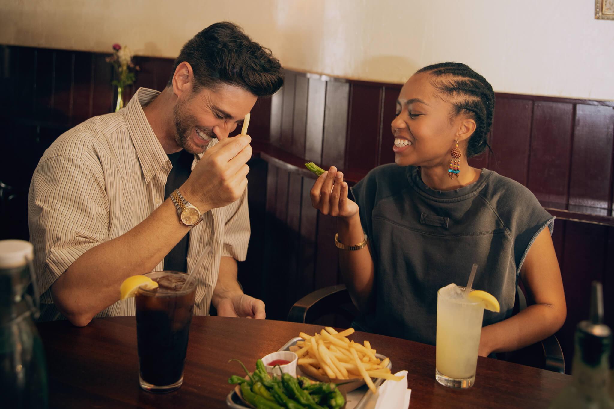 Casal sorridente a inclinar-se para um beijo e de mãos dadas no banco de trás de um carro, com verdura no exterior.