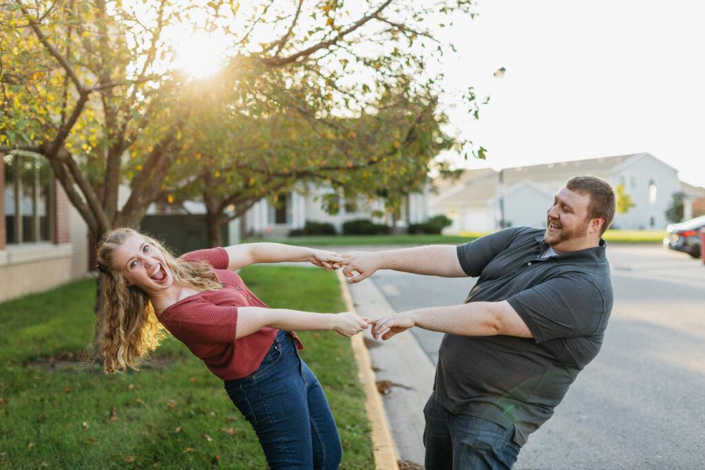 A photo of Emily and Kyle leaning back while holding hands. Emily is open-mouthed and looking excitedly at the camera while Kyle smiles at Emily. 