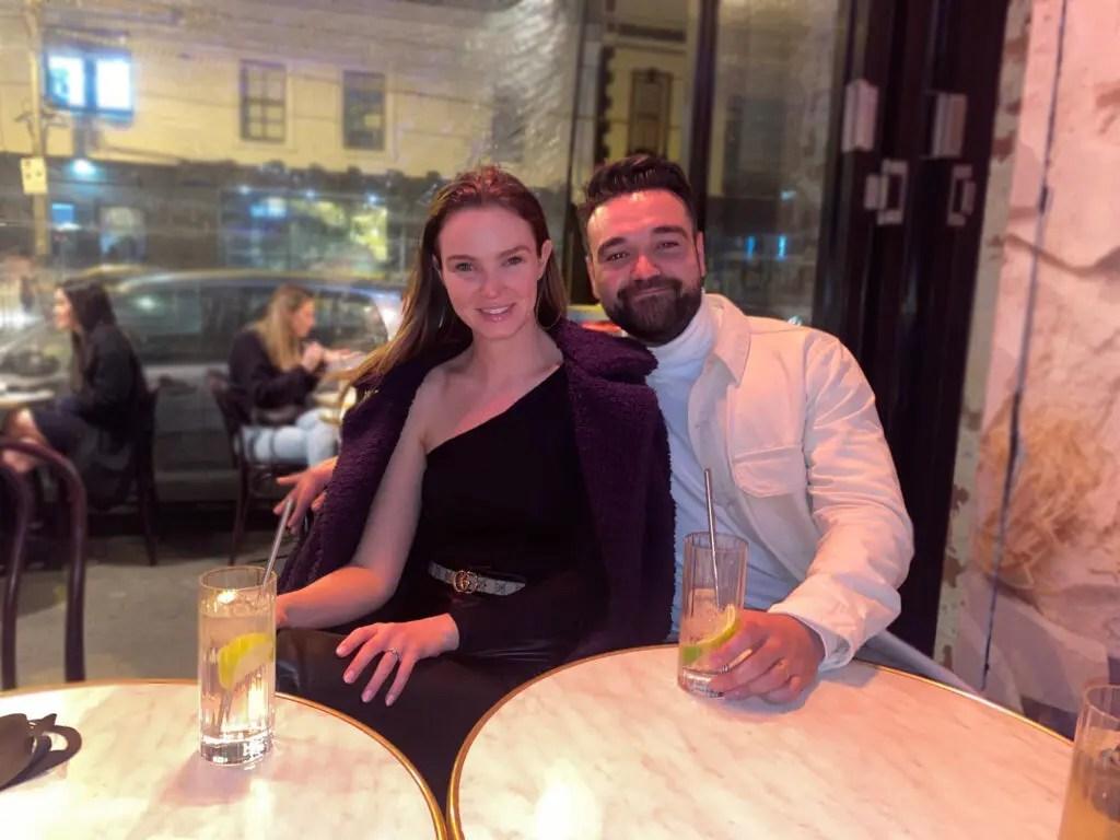 Luca and Bridie sitting at cafe tables with drinks.
