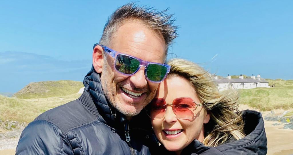Helen and Chris are standing close together on a windy beach. 