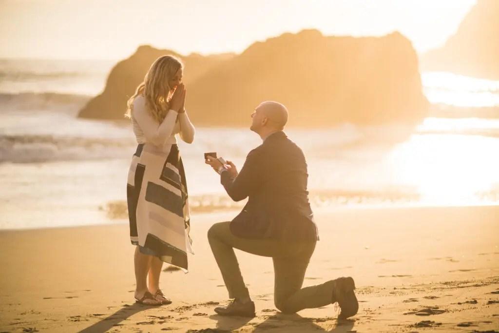 Adam proposing to Emily on a beach