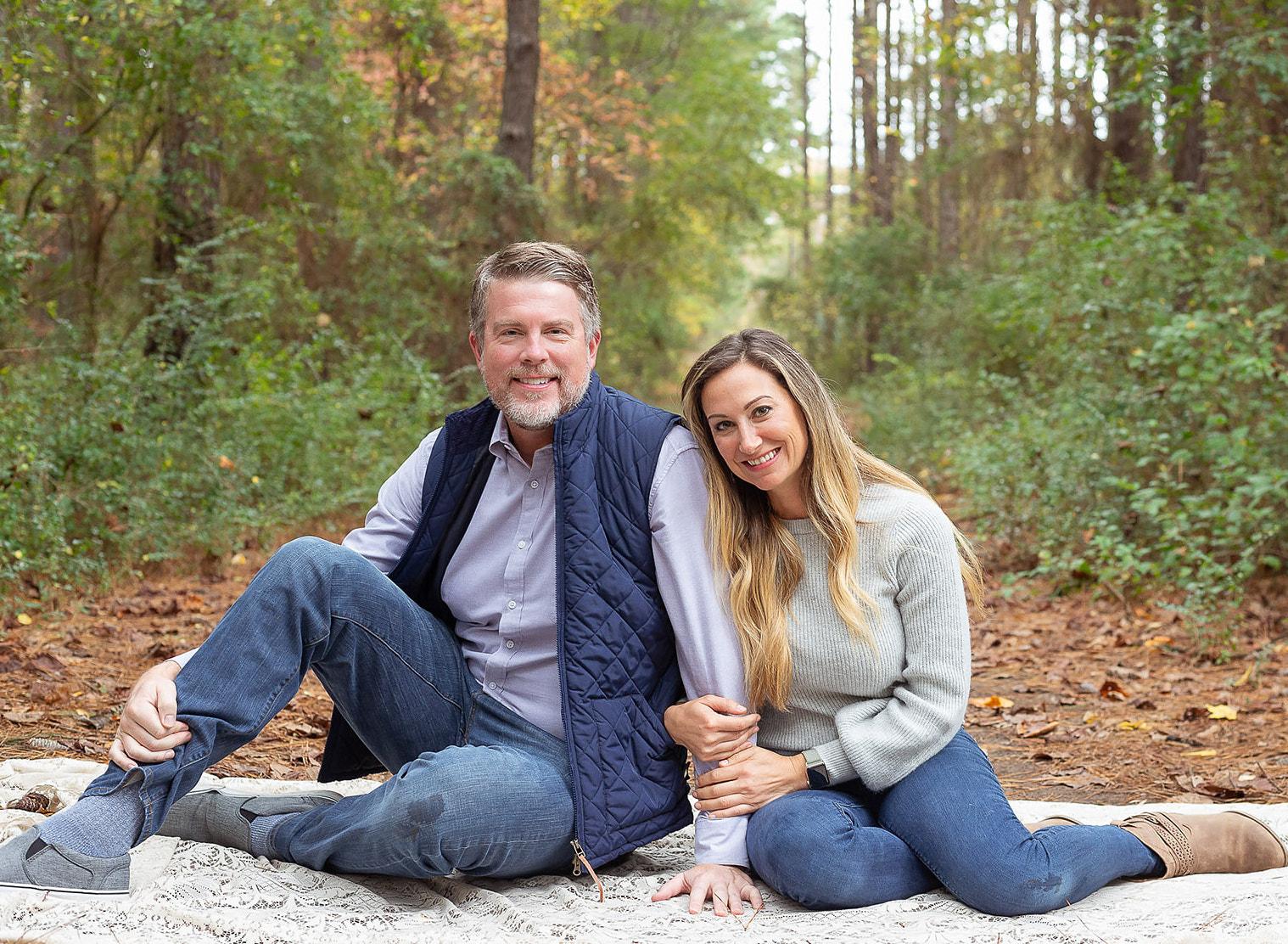 Jim and Meredith smiling and sitting down posing for a photo in a forest.