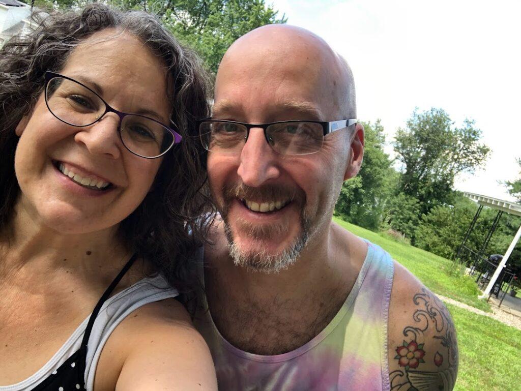 Wendy and Scott sat on some grass and taking a selfie, smiling at the camera.